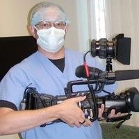 Person in medical scrubs holding a professional video camera.