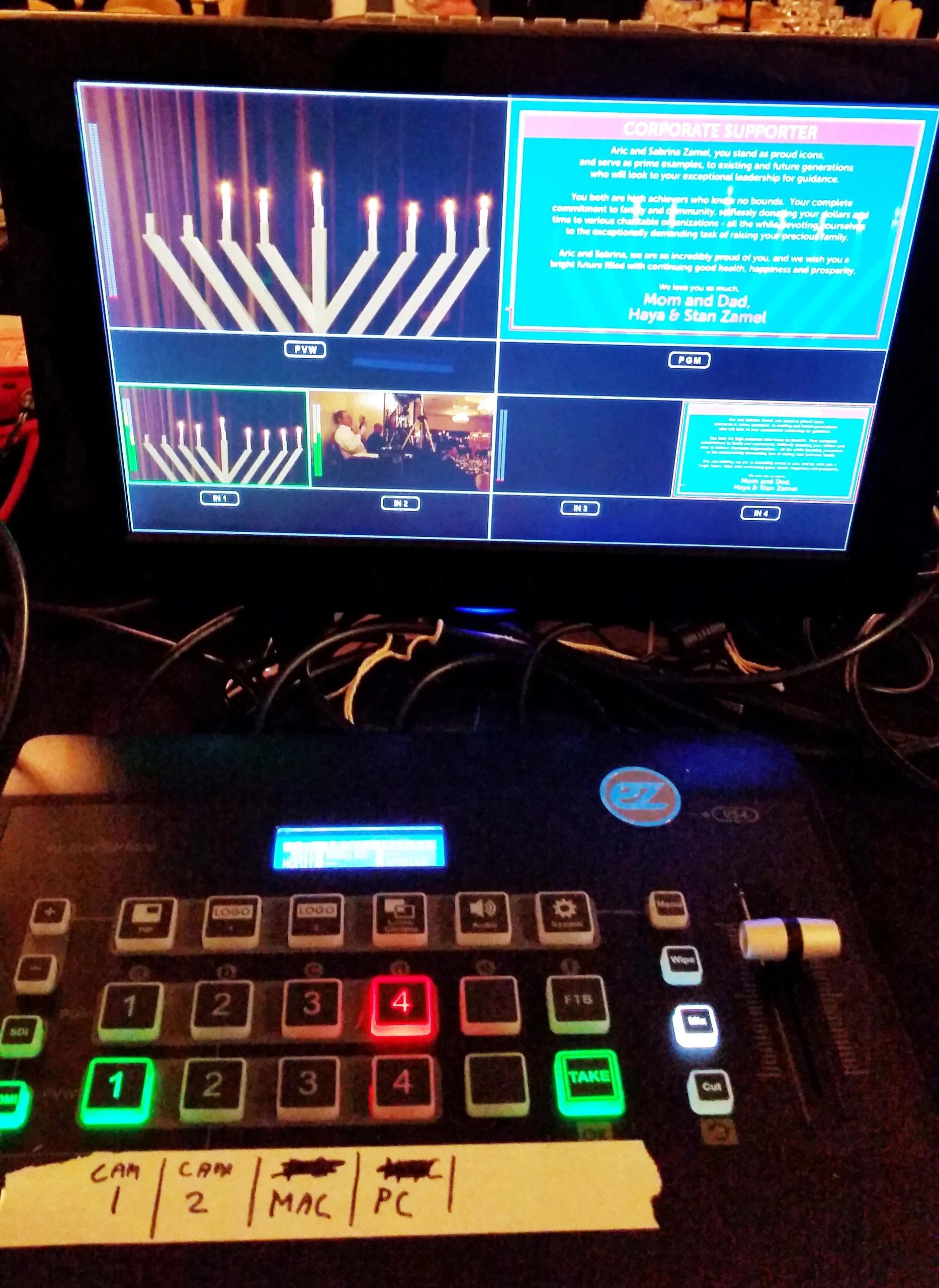 Close-up of a video switcher with illuminated buttons and a screen displaying multiple video feeds.